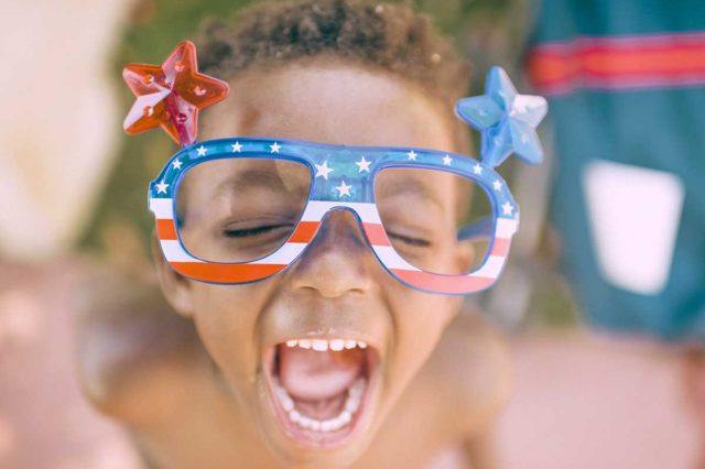 a young boy with patriotic sunglasses is yelling outside on a bright day