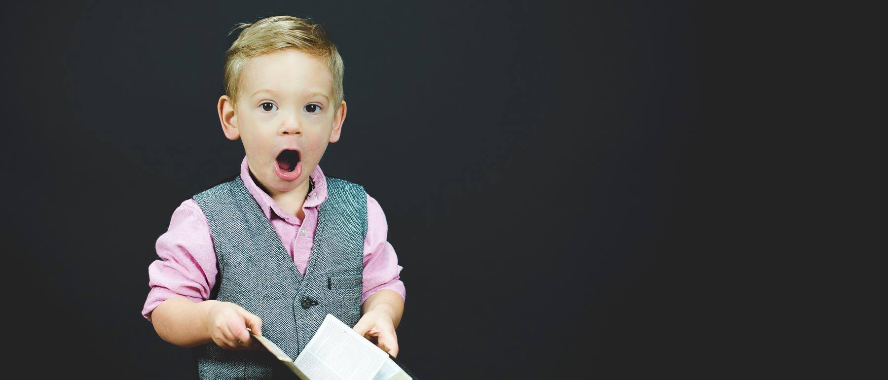 little boy in suit vest with shocked expression while holding book